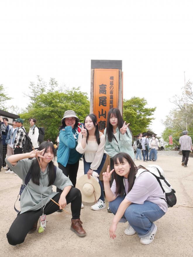 山頂の看板の前でポーズする学生たち
